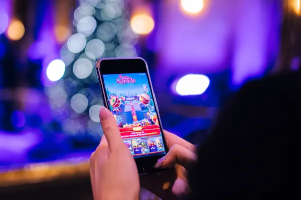 A young woman relaxing with her phone while dynamic casino elements float around her, illustrating the smooth mobile experience offered by the JL777 app.